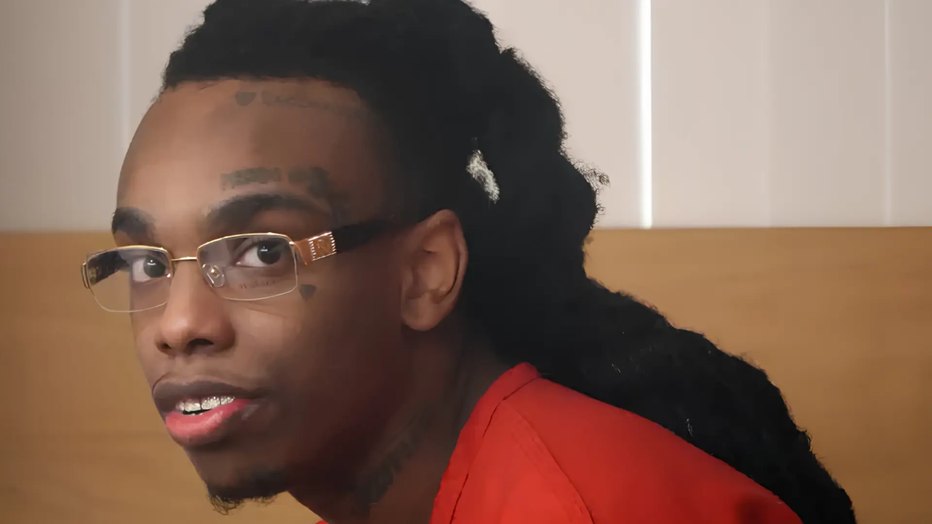 ynw-melly-been-in-jail-for-mugshot wearing glasses and a red shirt, looking to the side in an indoor setting.