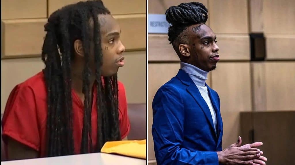 YNW melly in a courtroom shown with long dreadlocks in red shirt and with braided hair styled in a bun while wearing a blue suit.