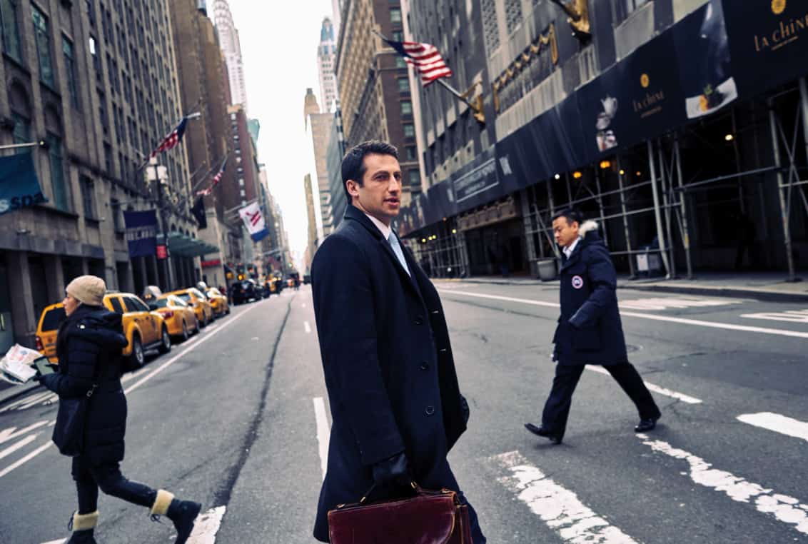 alex spiro walking across a city street carrying a briefcase