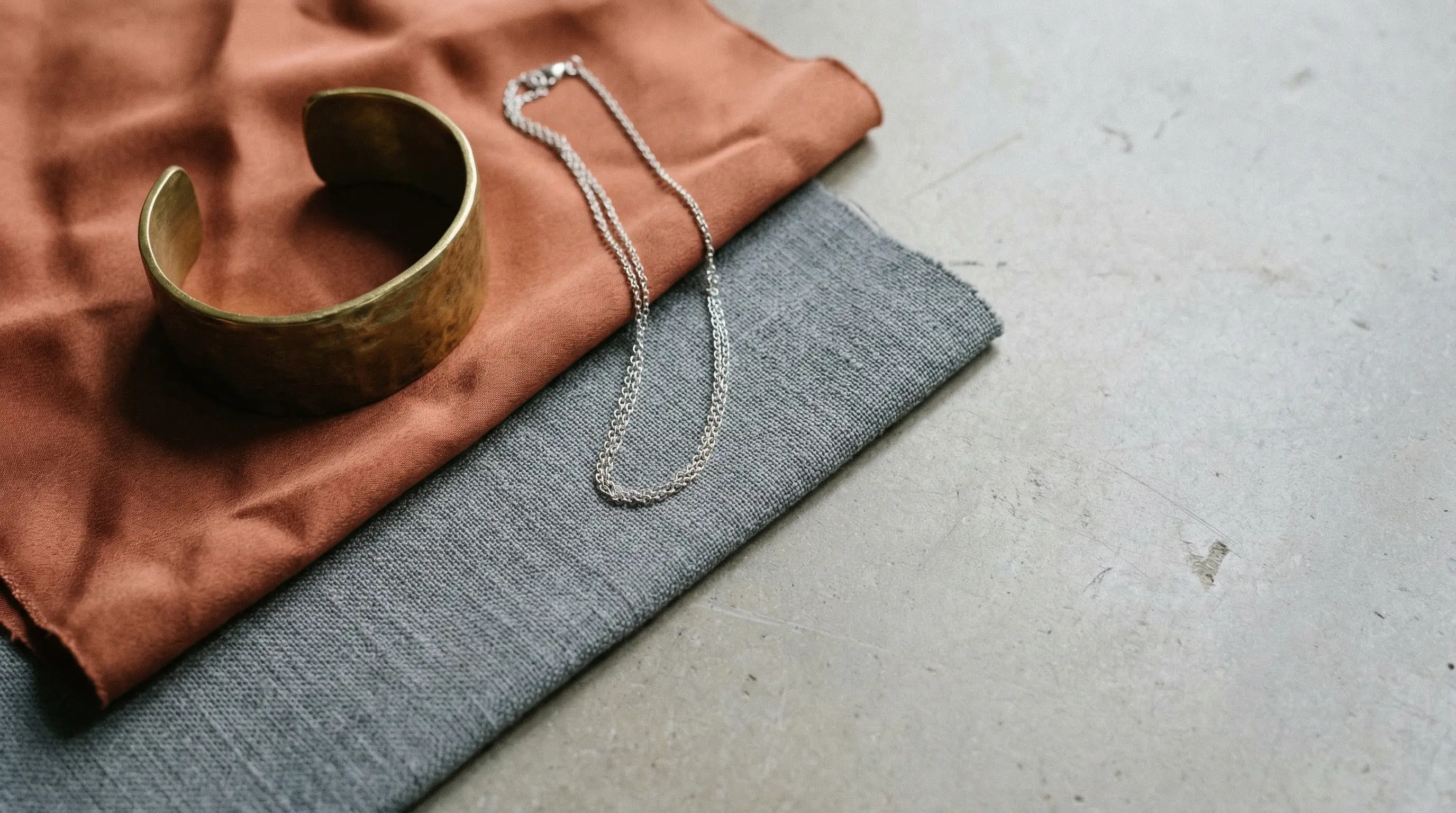 Bronze cuff bracelet and silver chain necklace on beige and gray fabric surfaces
