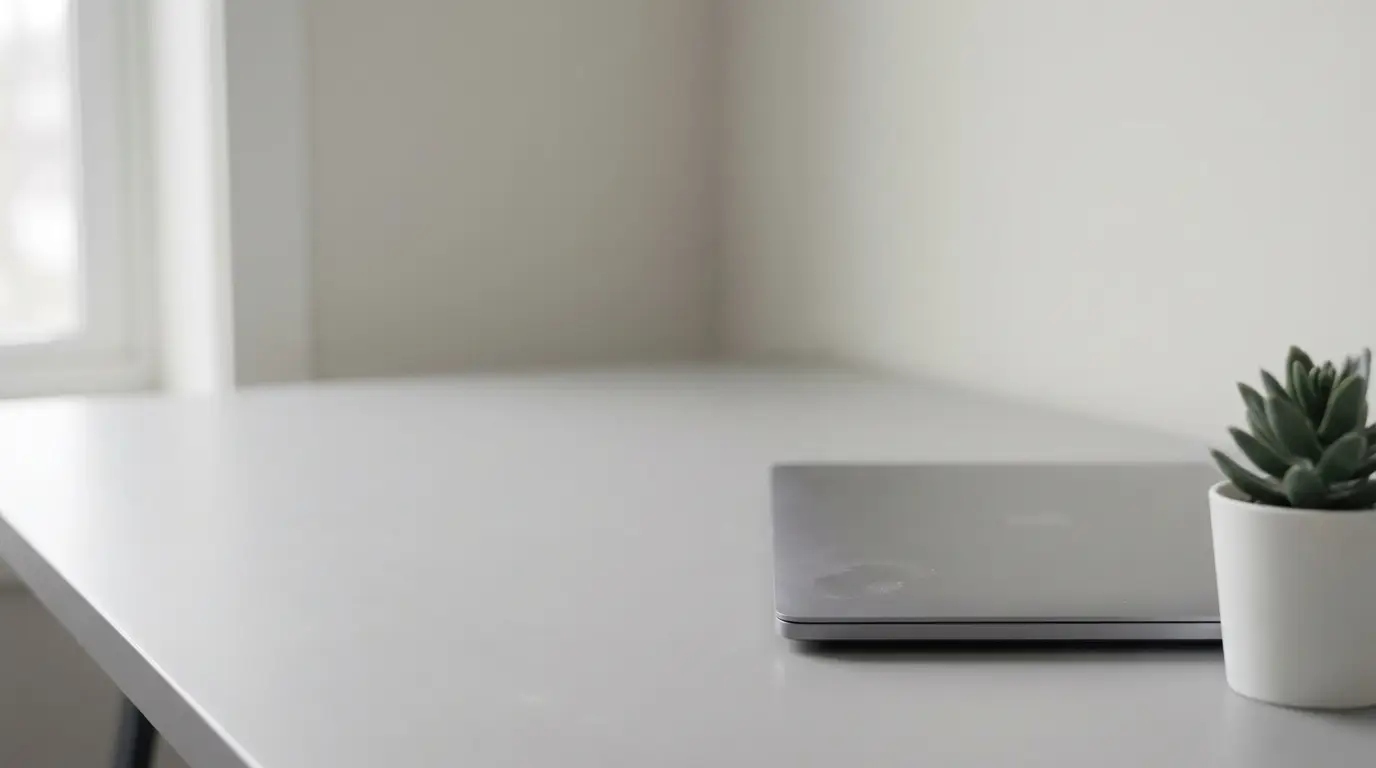 Closed laptop and small potted plant on minimalist white desk near window