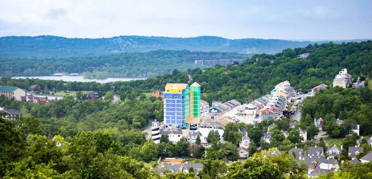 Colorful buildings nestled among green hills with distant lake and hilly backdrop