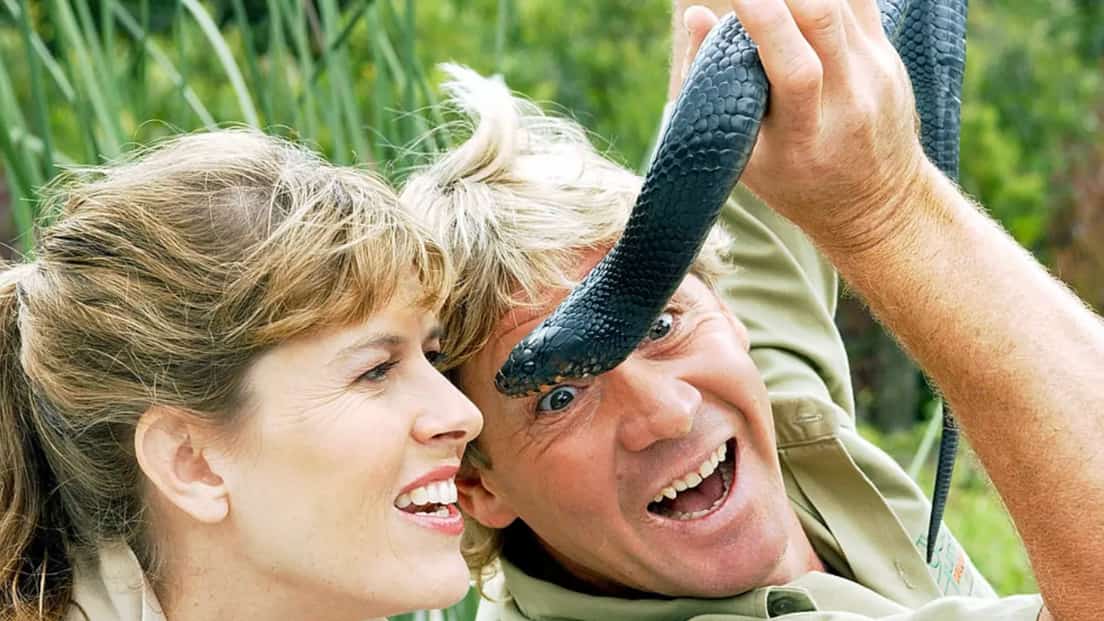 steve-irwin-holding-a-black snake close to his face with his wife beside him
