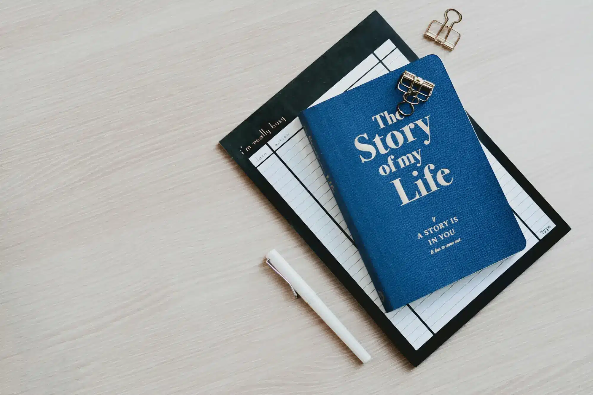 Blue notebook titled "The Story of My Life" on clipboard with pen on wooden surface