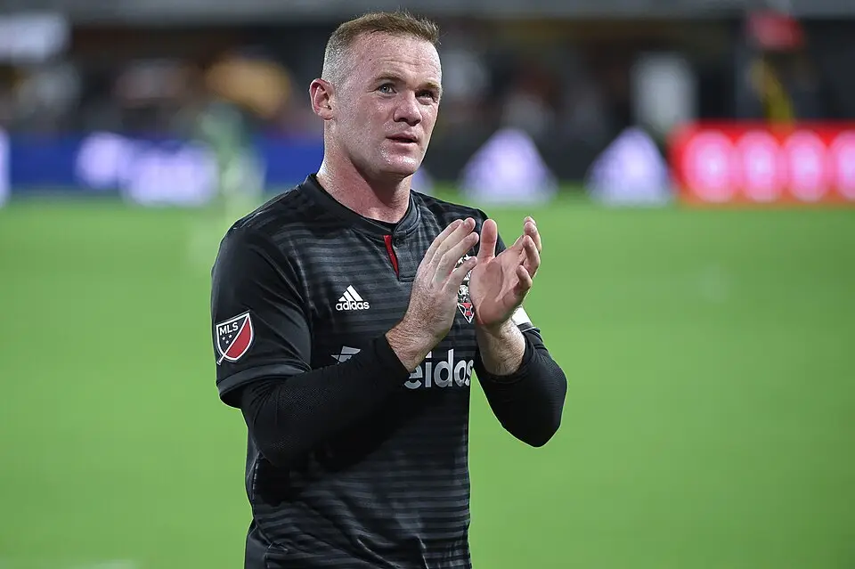 Soccer player in black jersey clapping on field under stadium lights