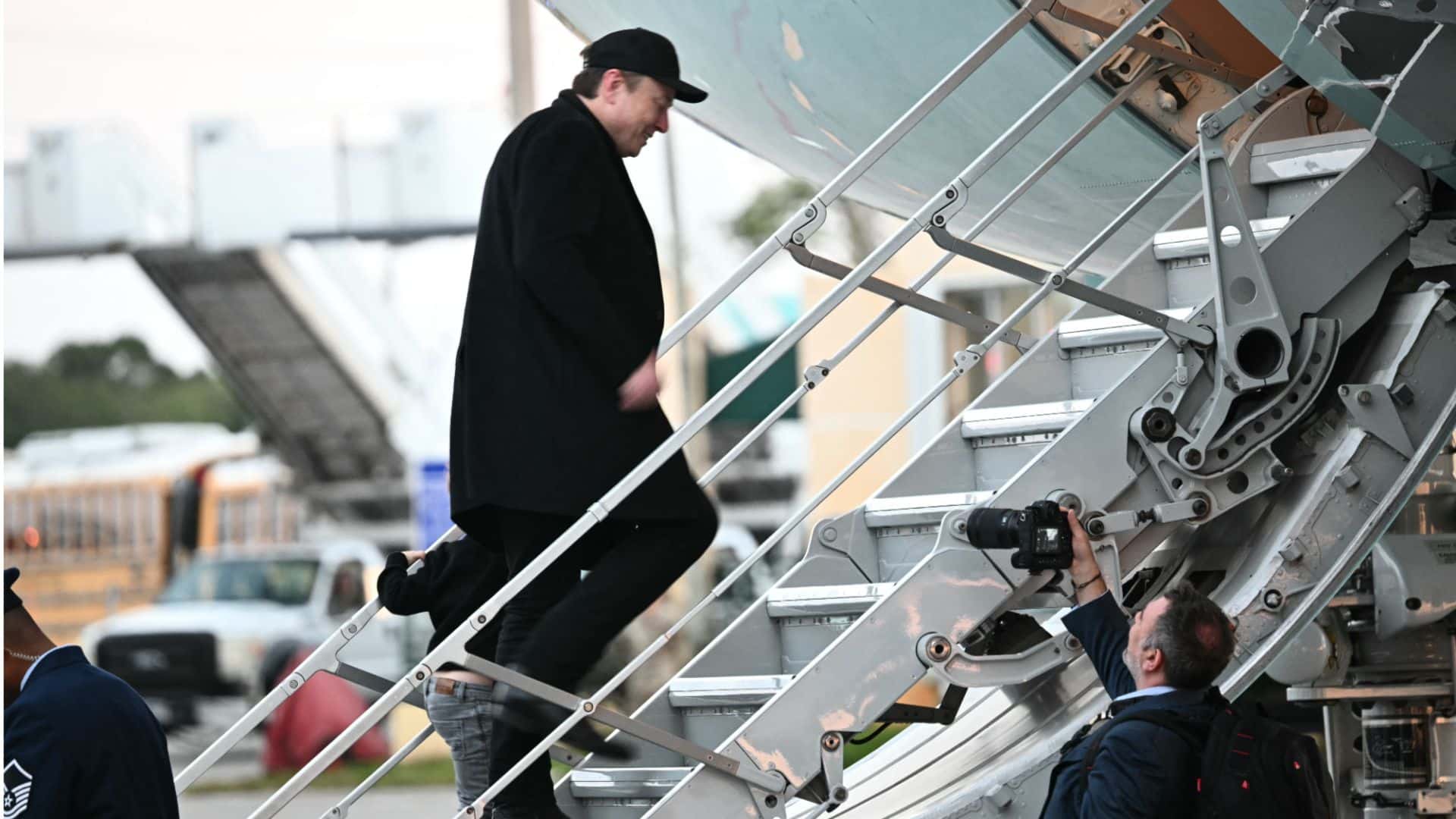 Elon Musk Climbing the Stairs to Board His Private Jet While a Photographer Captures the Moment Below.