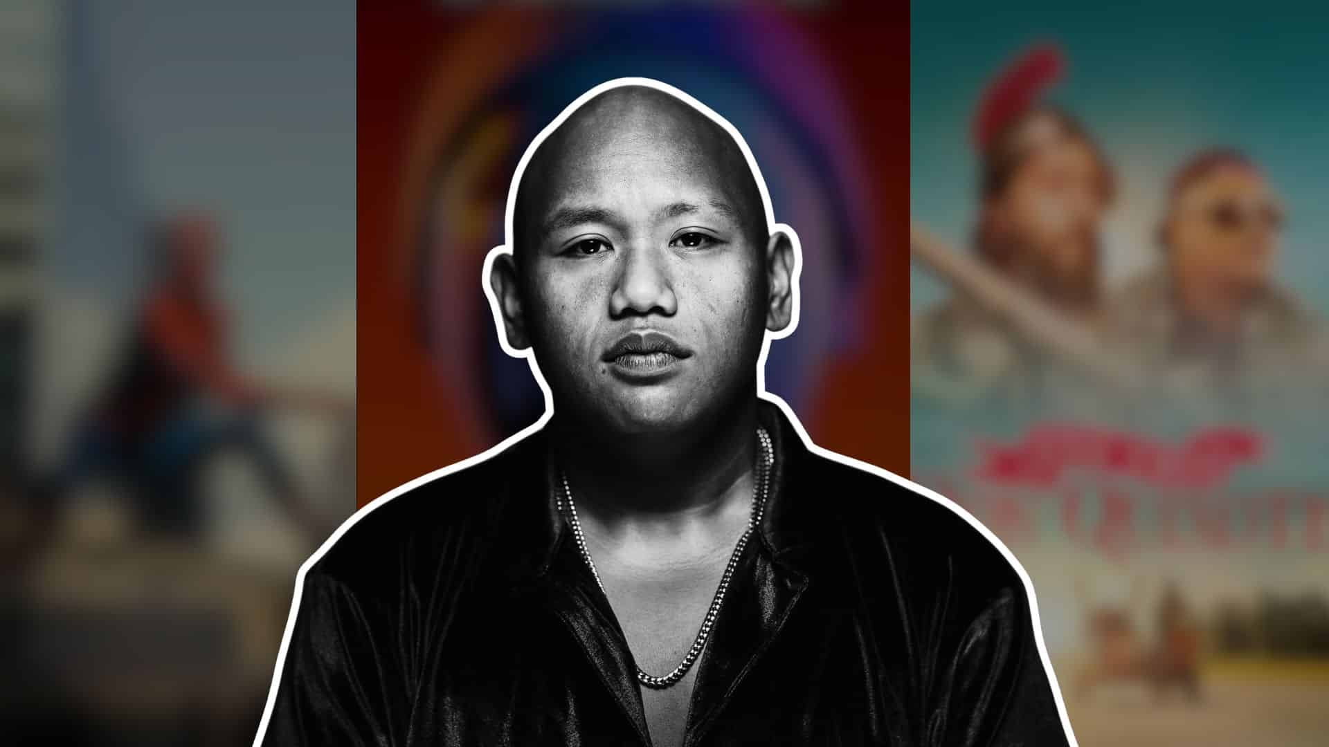 Jacob Batalon in a black-and-white portrait, wearing a dark jacket and chain necklace against a blurred background.