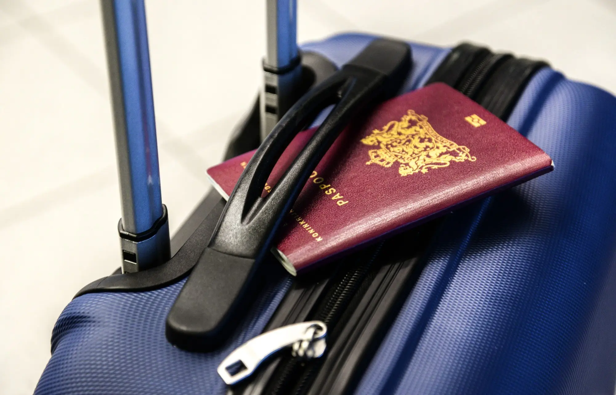 Passport resting on closed blue suitcase with telescopic handle in tiled setting