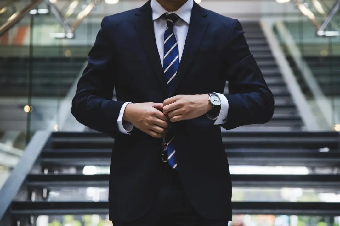 Man in formal suit adjusting tie on indoor staircase with glass railing