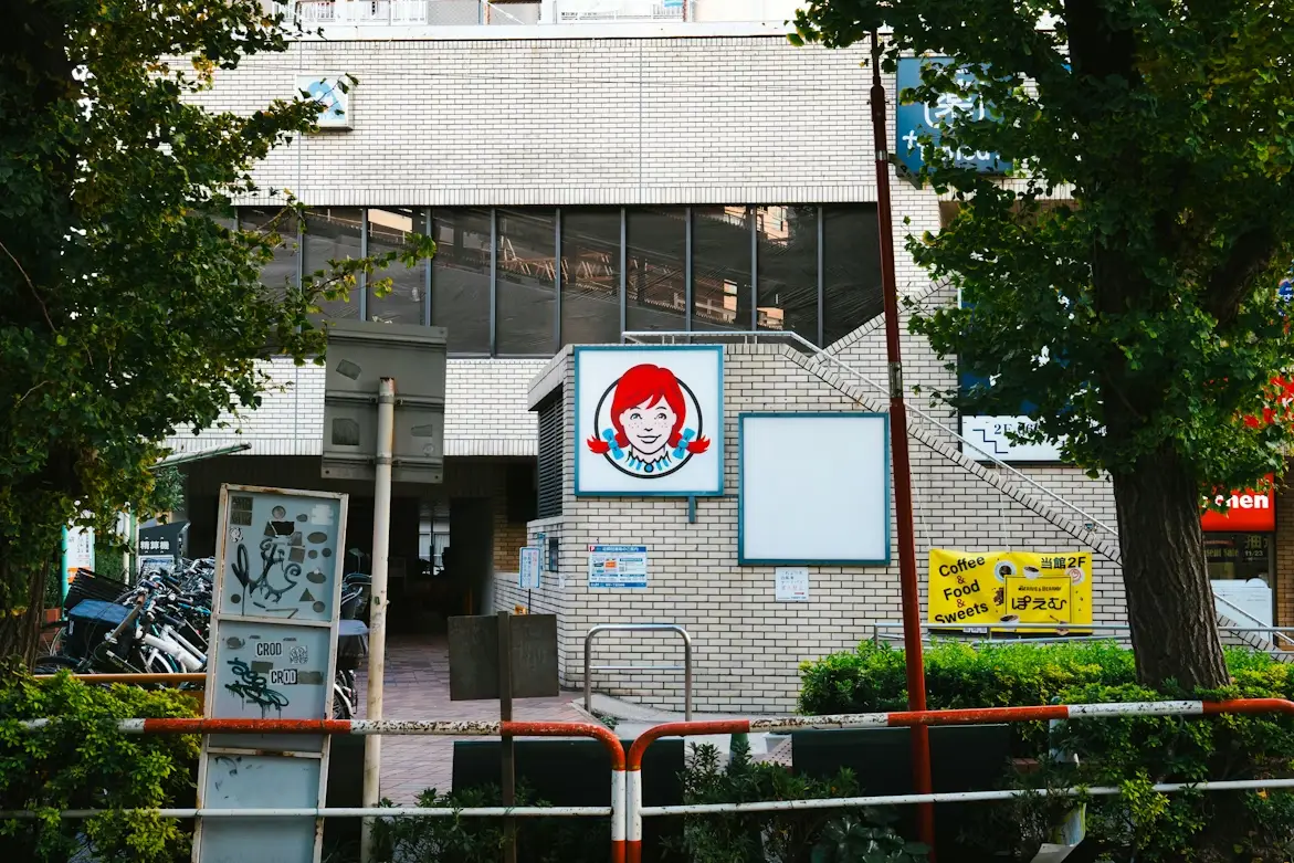 Red-haired cartoon logo on building exterior beside trees and bicycles in urban setting