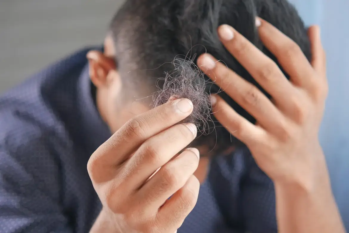 Man holding clump of hair while touching head indoors