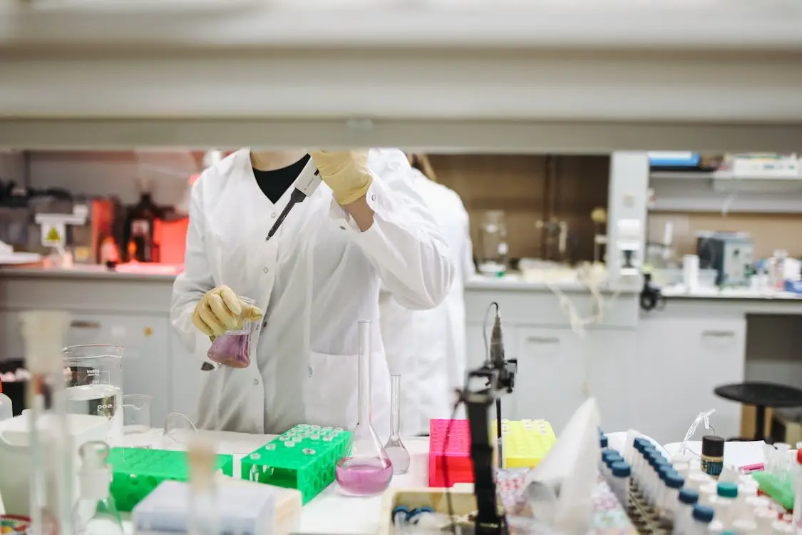 Scientist in white lab coat using pipette in a laboratory with colorful test tube racks