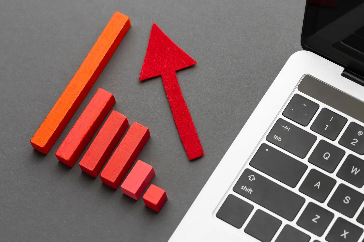 Red bar graph and felt arrow next to a laptop keyboard on a gray background