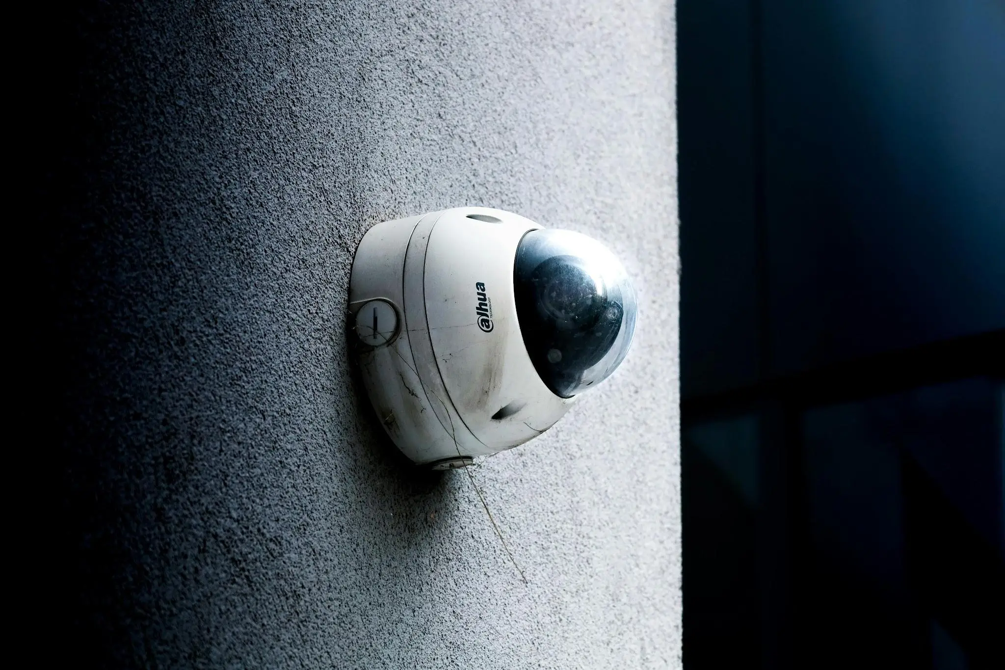 Security camera mounted on textured concrete wall under dim lighting