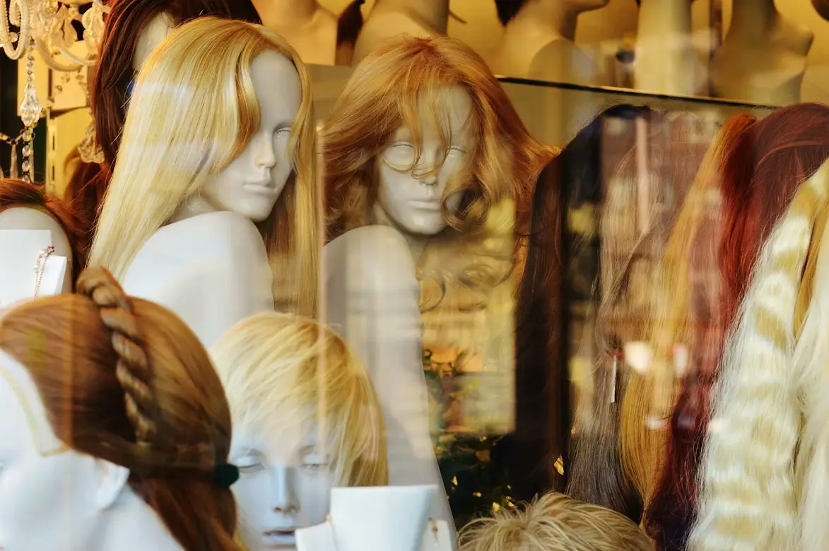 Mannequins with various wigs displayed in shop window with warm lighting