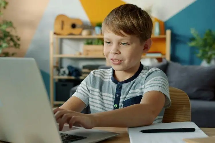 Young boy using laptop at wooden desk in colorful home office setting