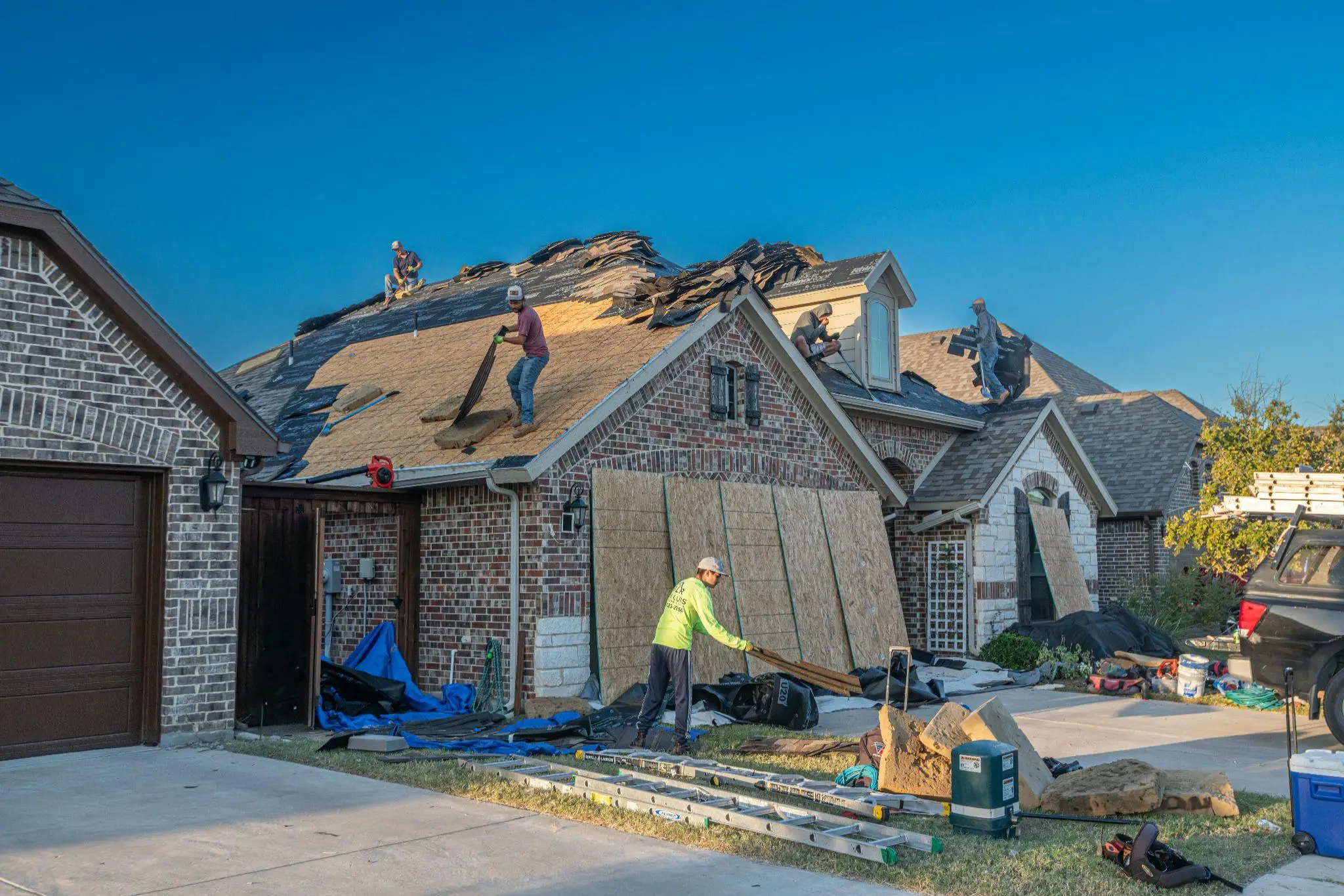 Roofers working on installing new shingles on suburban home under clear sky