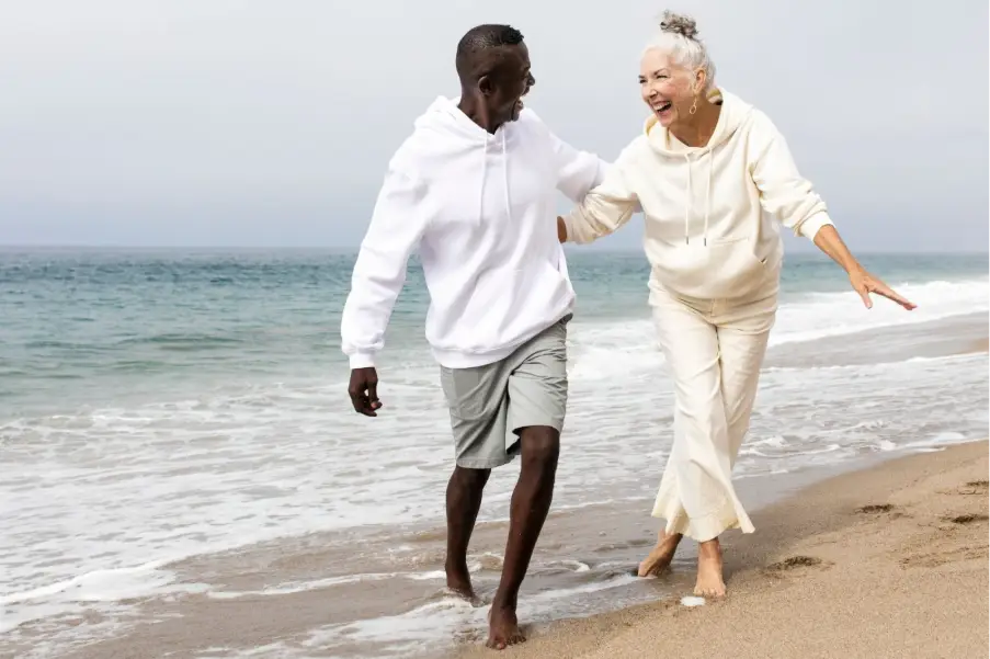 Couple in casual hoodies walking along sandy beach near ocean waves