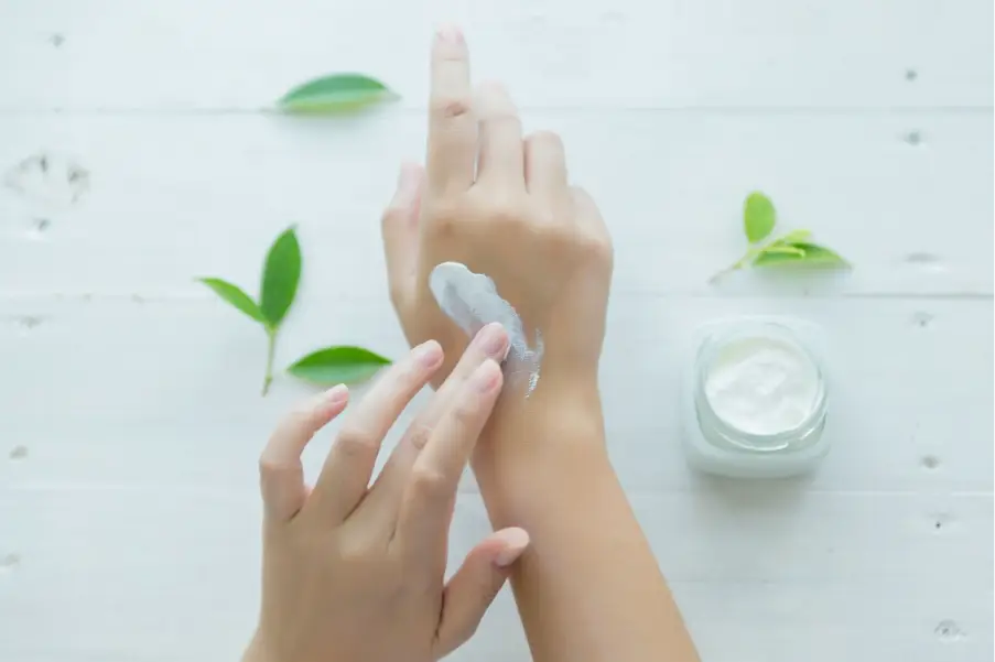 Applying cream to hand on white wooden table with green leaves nearby