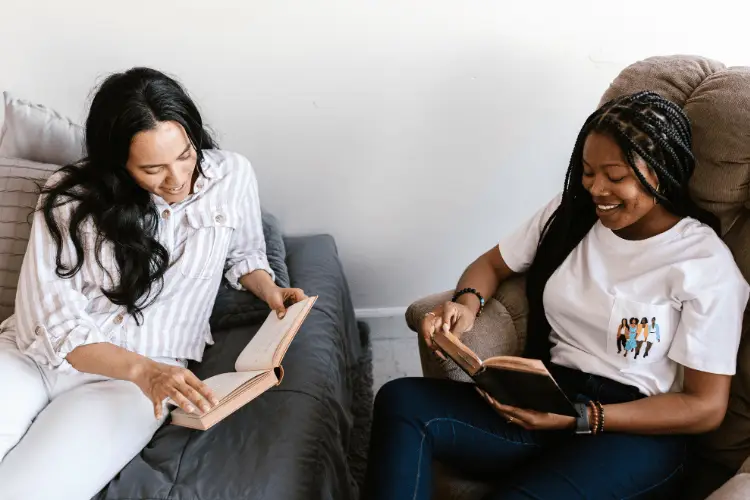 Two women reading books together in a cozy living room setting