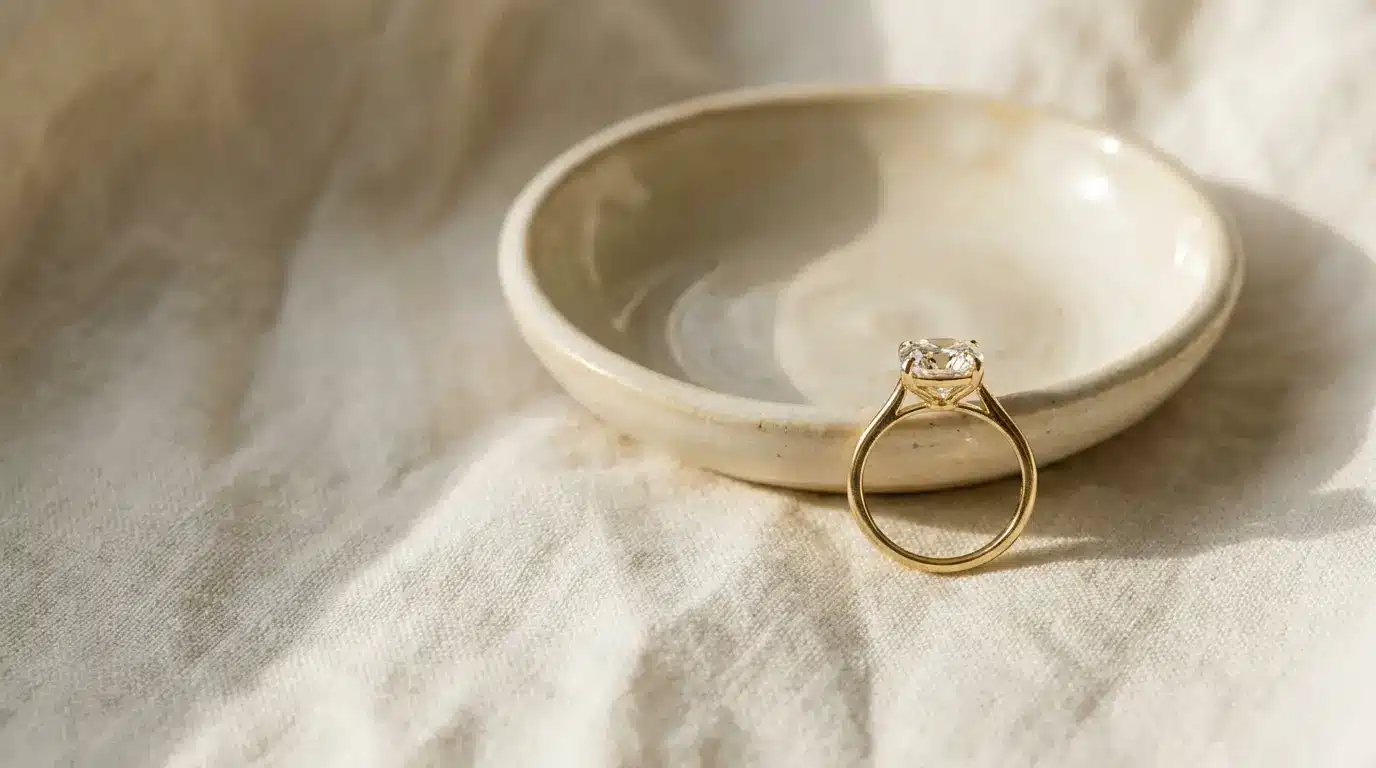Gold ring with gemstone displayed on ceramic dish under soft natural light
