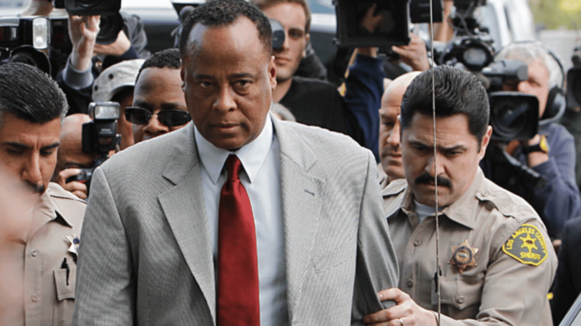 Dr. Conrad Murray arriving at court surrounded by reporters and police.