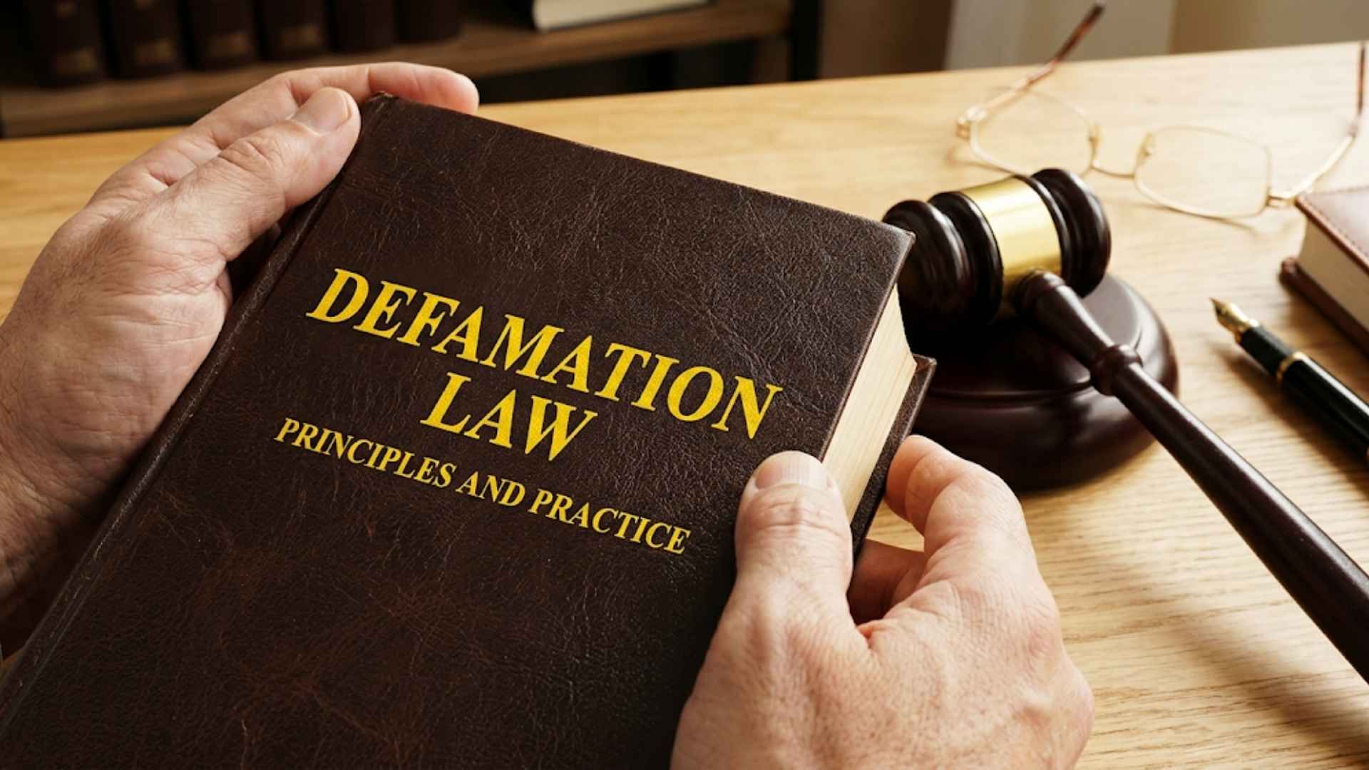 A person holding a legal book titled Defamation Law next to a judge's gavel.