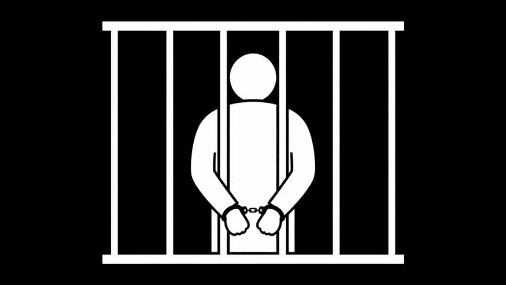 Silhouetted person in handcuffs behind prison bars, representing incarceration and legal consequences.