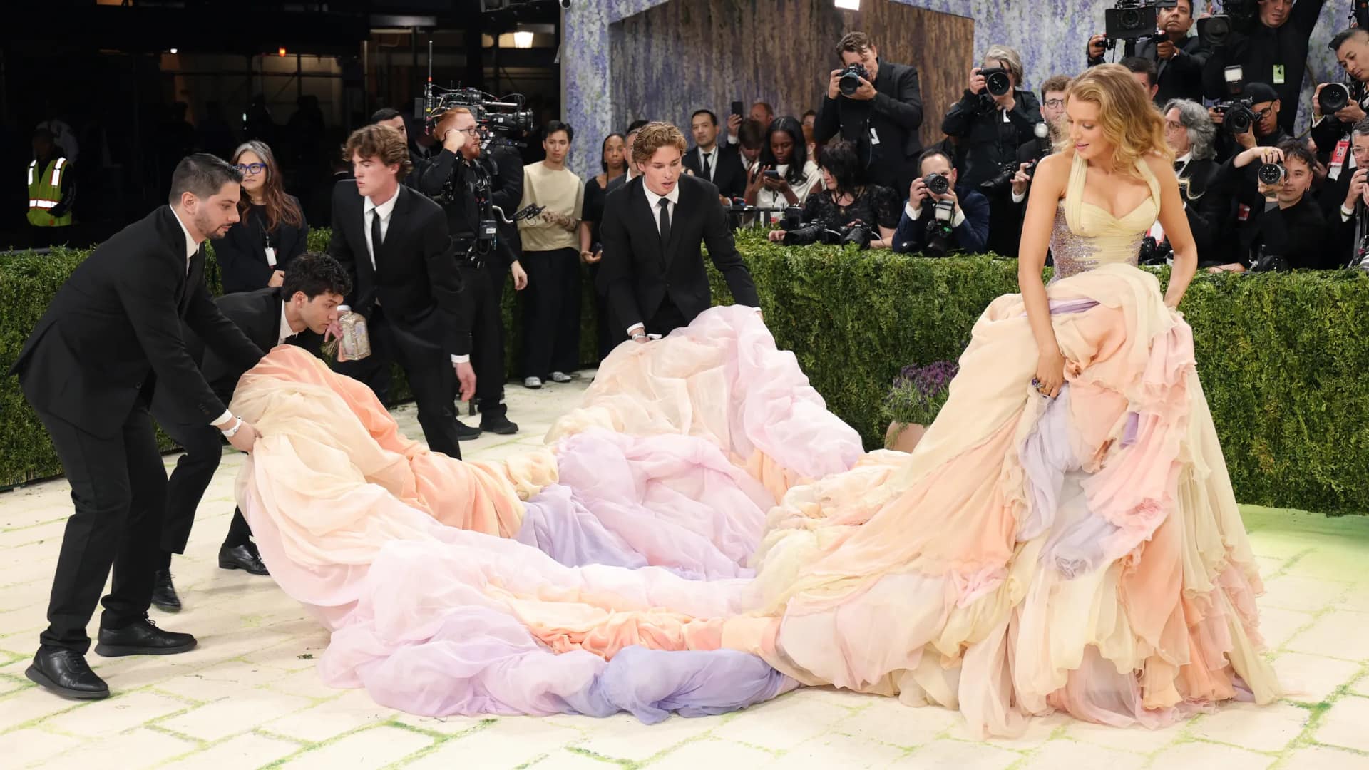 Blake Lively adjusting her pastel Versace gown with assistants during the 2022 Met Gala red carpet reveal.