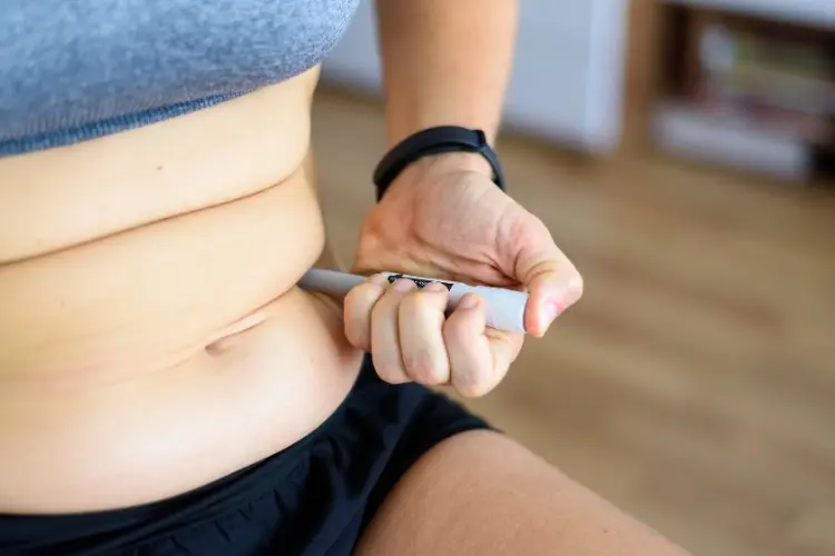 Person pinching abdominal skin and holding grey measuring tool in bright indoor setting