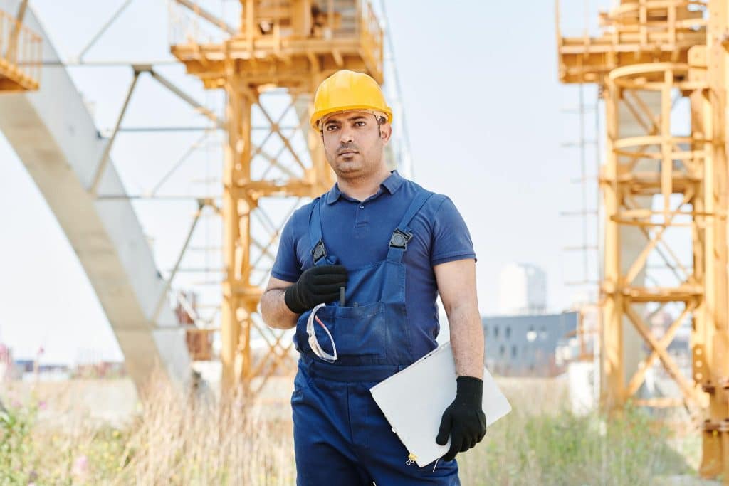 Man in safety gear holding blueprint on construction site with cranes