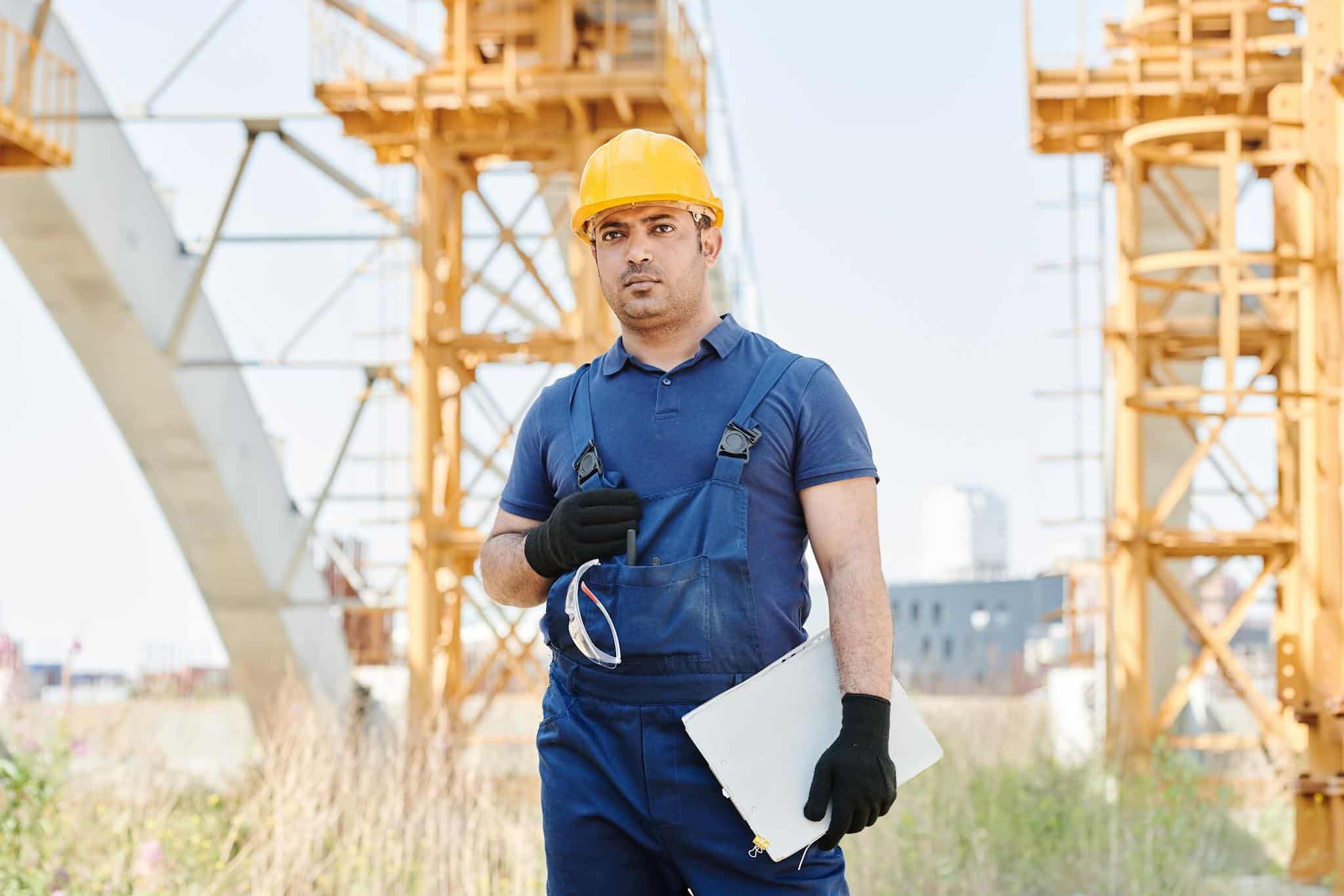 Man in safety gear holding blueprint on construction site with cranes