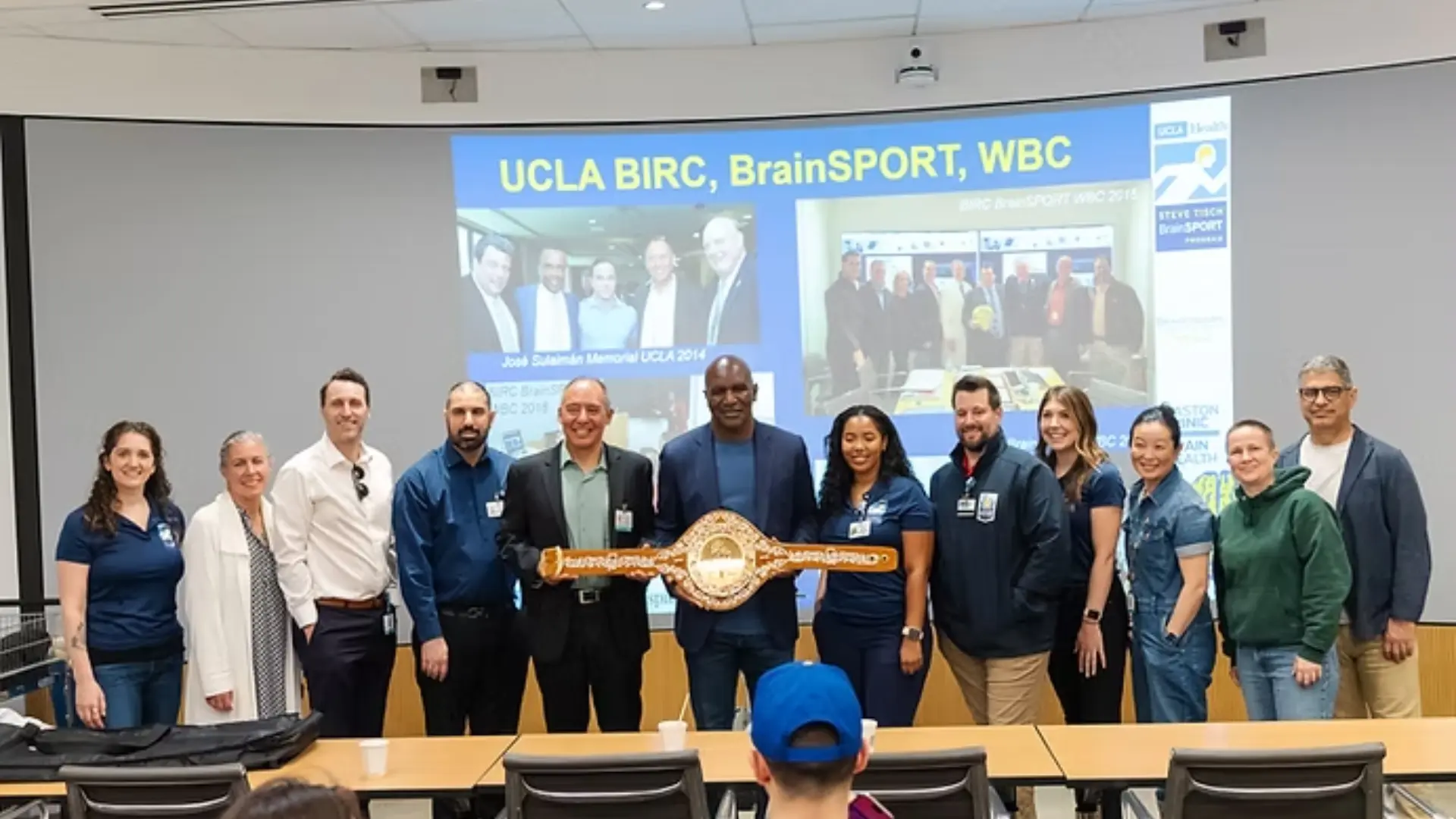 Evander Holyfield stands with a championship belt alongside researchers and staff during a group photo at a UCLA BrainSPORT event.