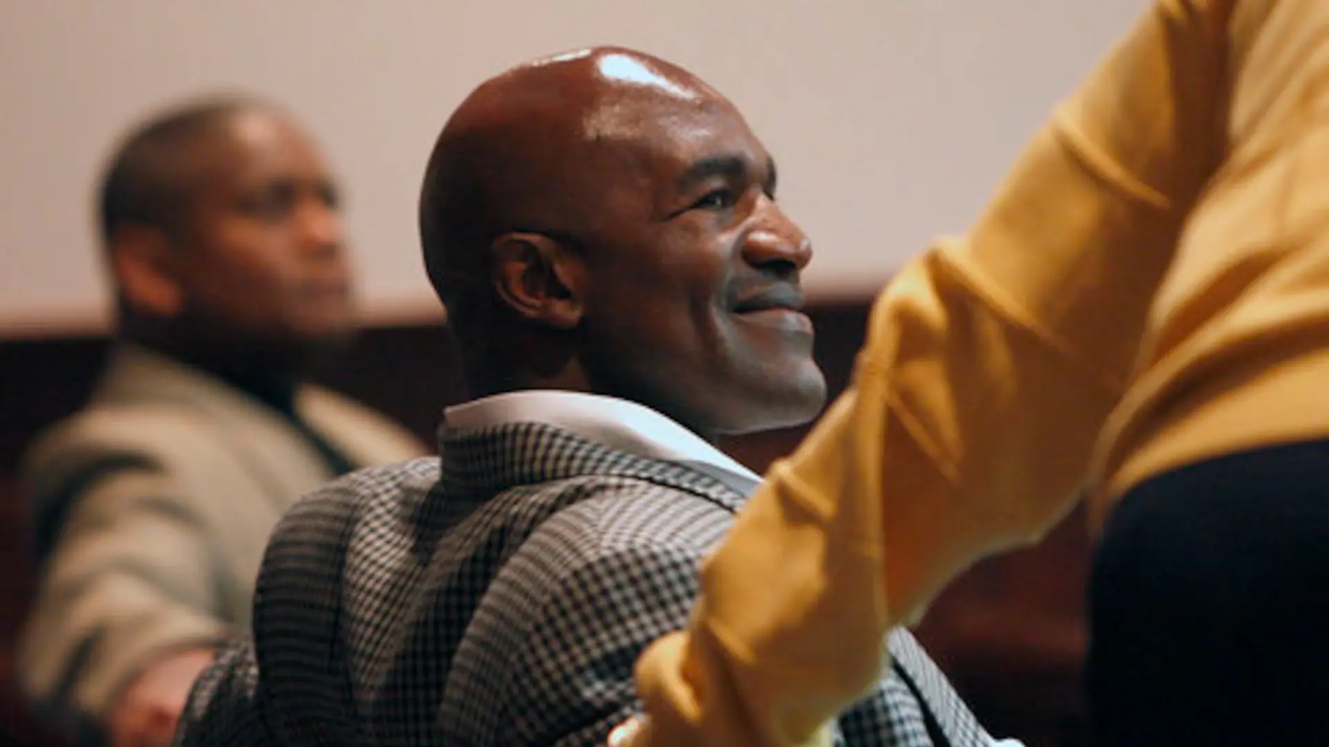Evander Holyfield smiles while attending a formal event, seated among other guests in an indoor venue.