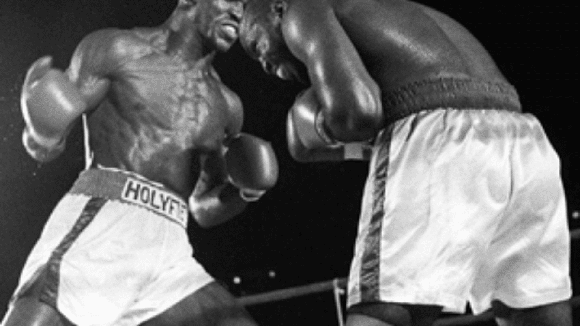 Evander Holyfield in a close-range exchange during a boxing match, both fighters wearing gloves and white trunks inside the ring