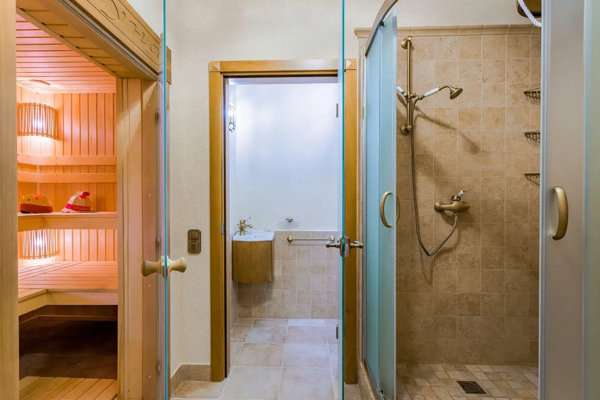 Sauna room with wooden interior next to a tiled shower and small washroom in bright light
