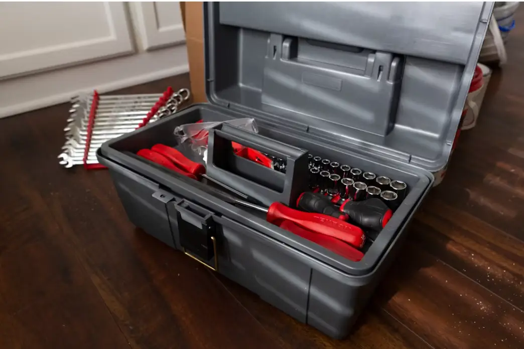 Open toolbox with red-handled tools and socket set on dark wooden floor