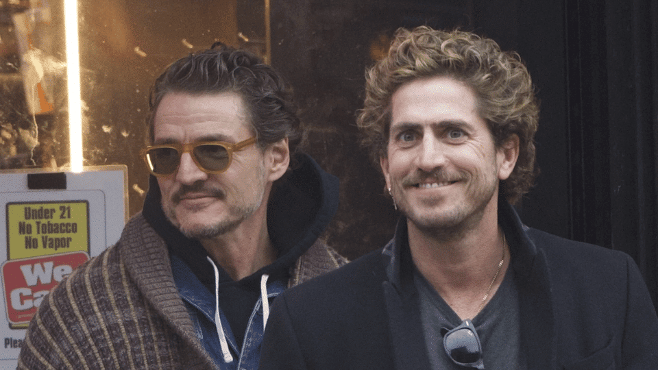 Rafael Olarra standing outdoors beside pedro pascal in sunglasses and scarf, both posing in casual street style attire.