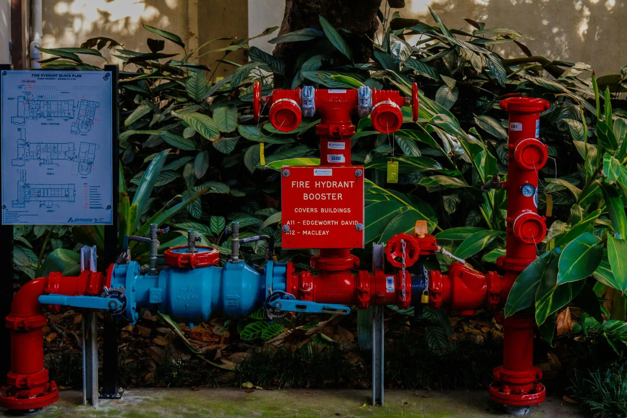 Red fire hydrant booster system with valves and sign in lush garden setting