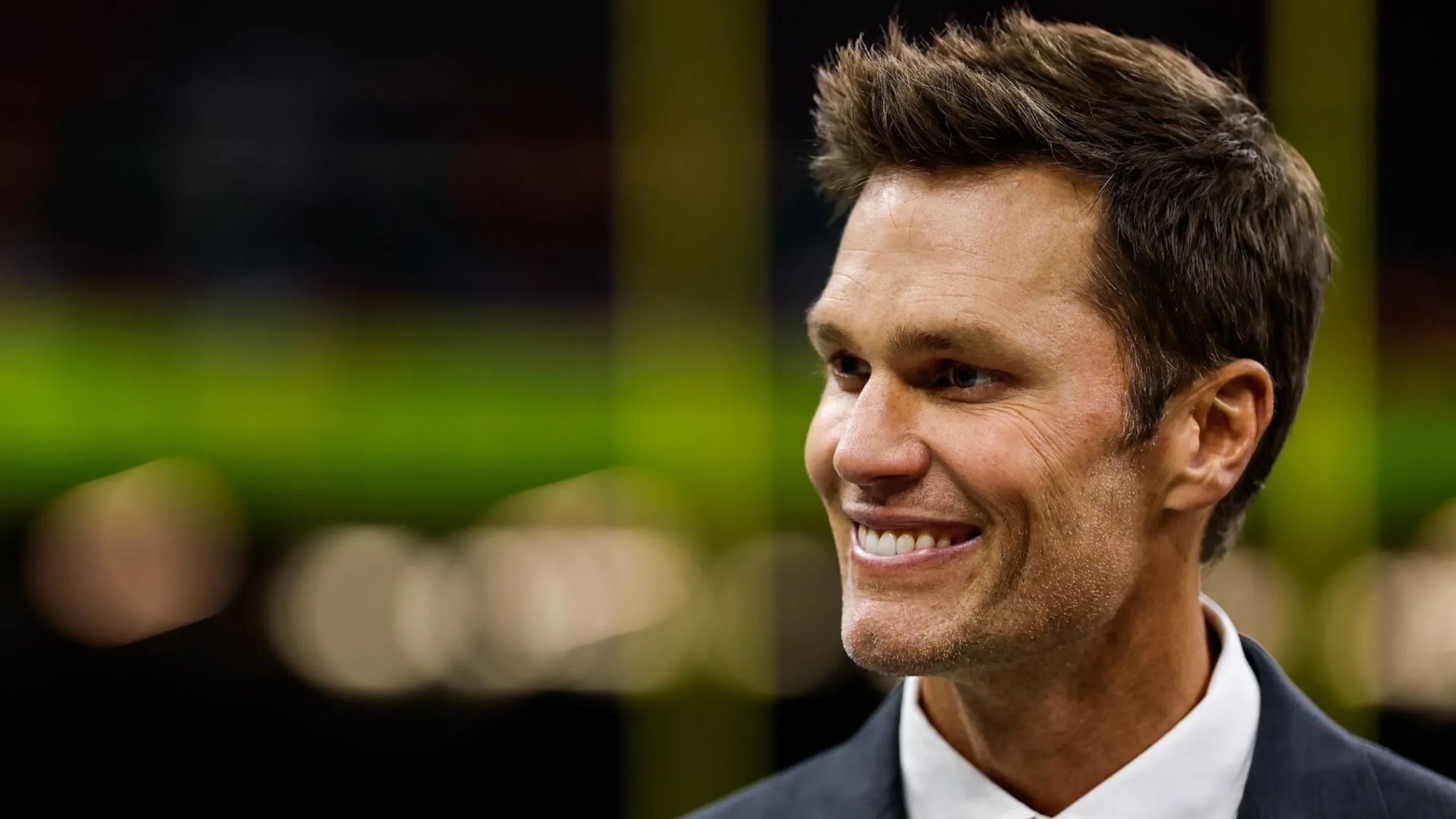 Tom Brady smiling in a suit during a public appearance
