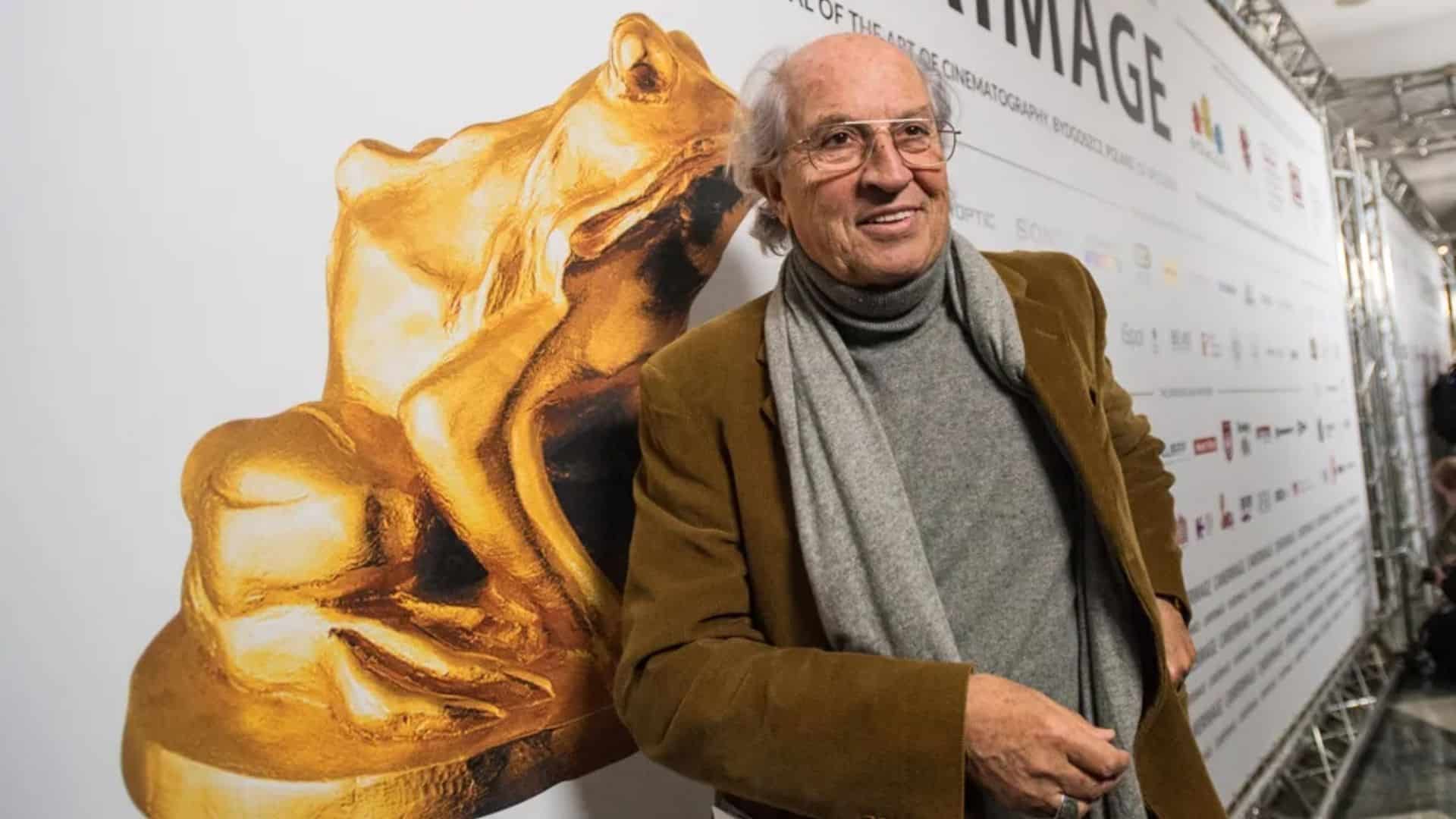 Vittorio Storaro posing beside a golden bear statue at a film event backdrop