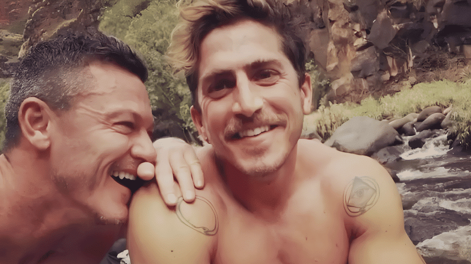 Luke Evans and Rafael Olarra smiling shirtless outdoors by a rocky river