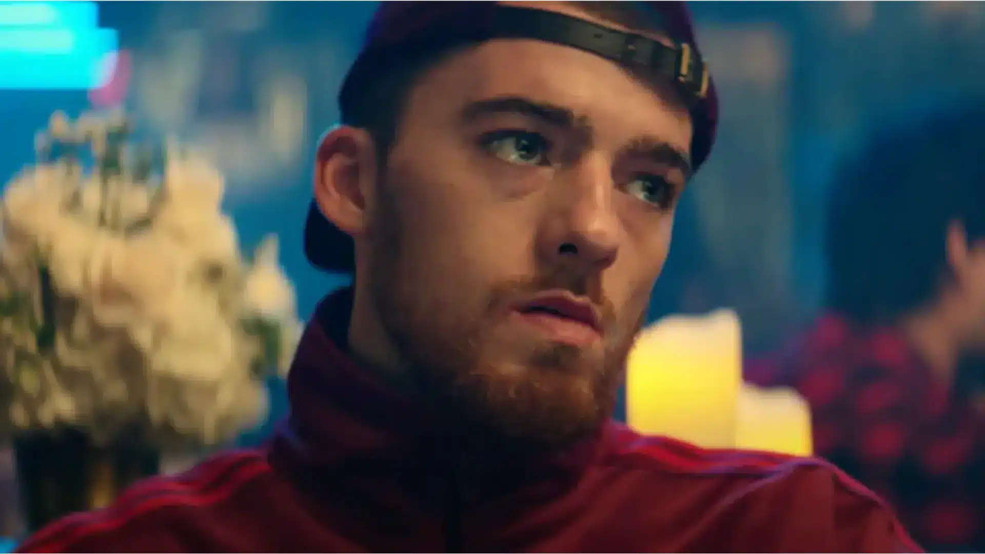 Angus Cloud appearing in a music video, dressed in stylish casual attire, standing on set with moody lighting, capturing his relaxed and charismatic presence on camera.