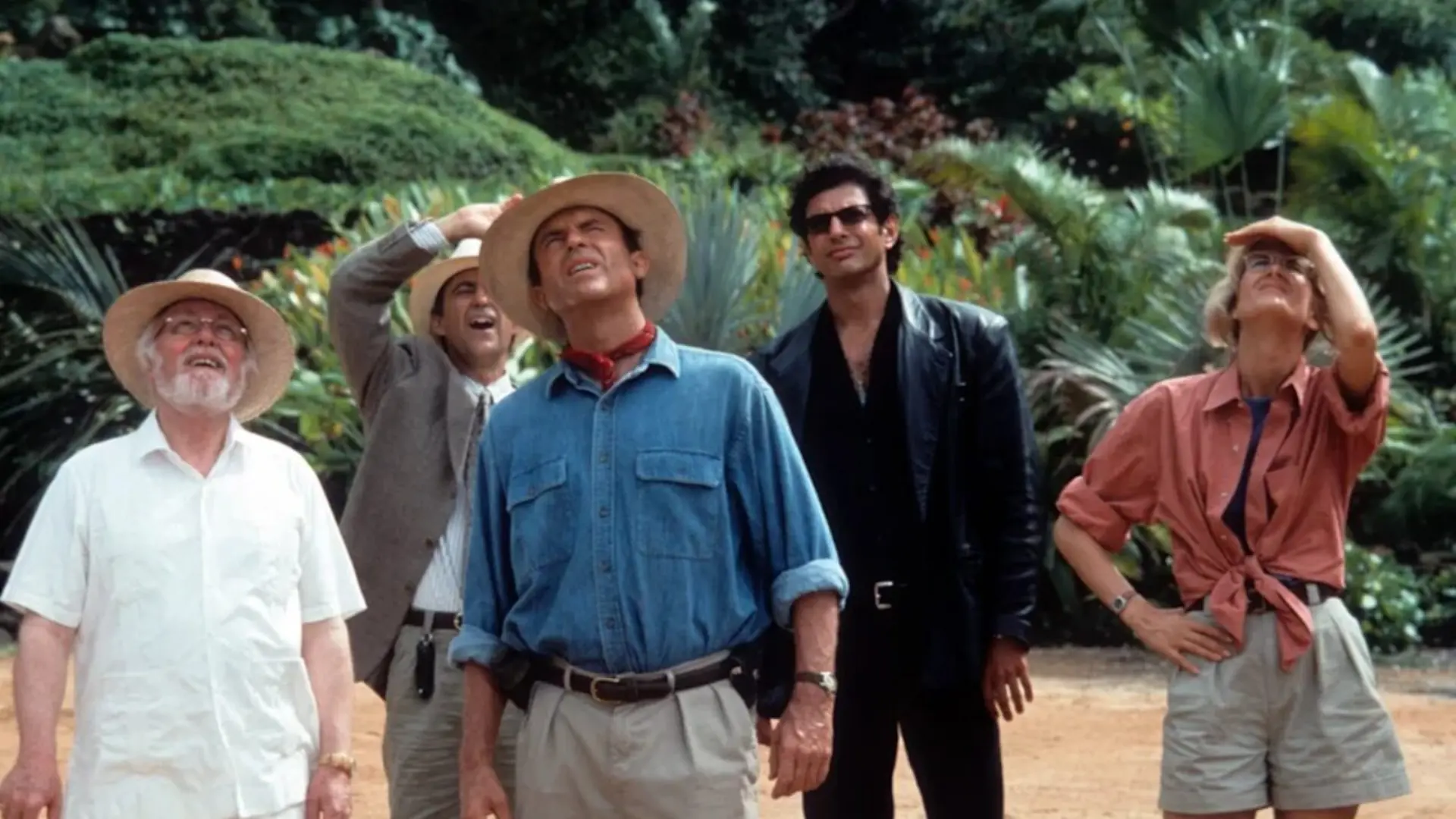 Sam Neill and Jurassic Park cast members looking up together in a jungle scene.