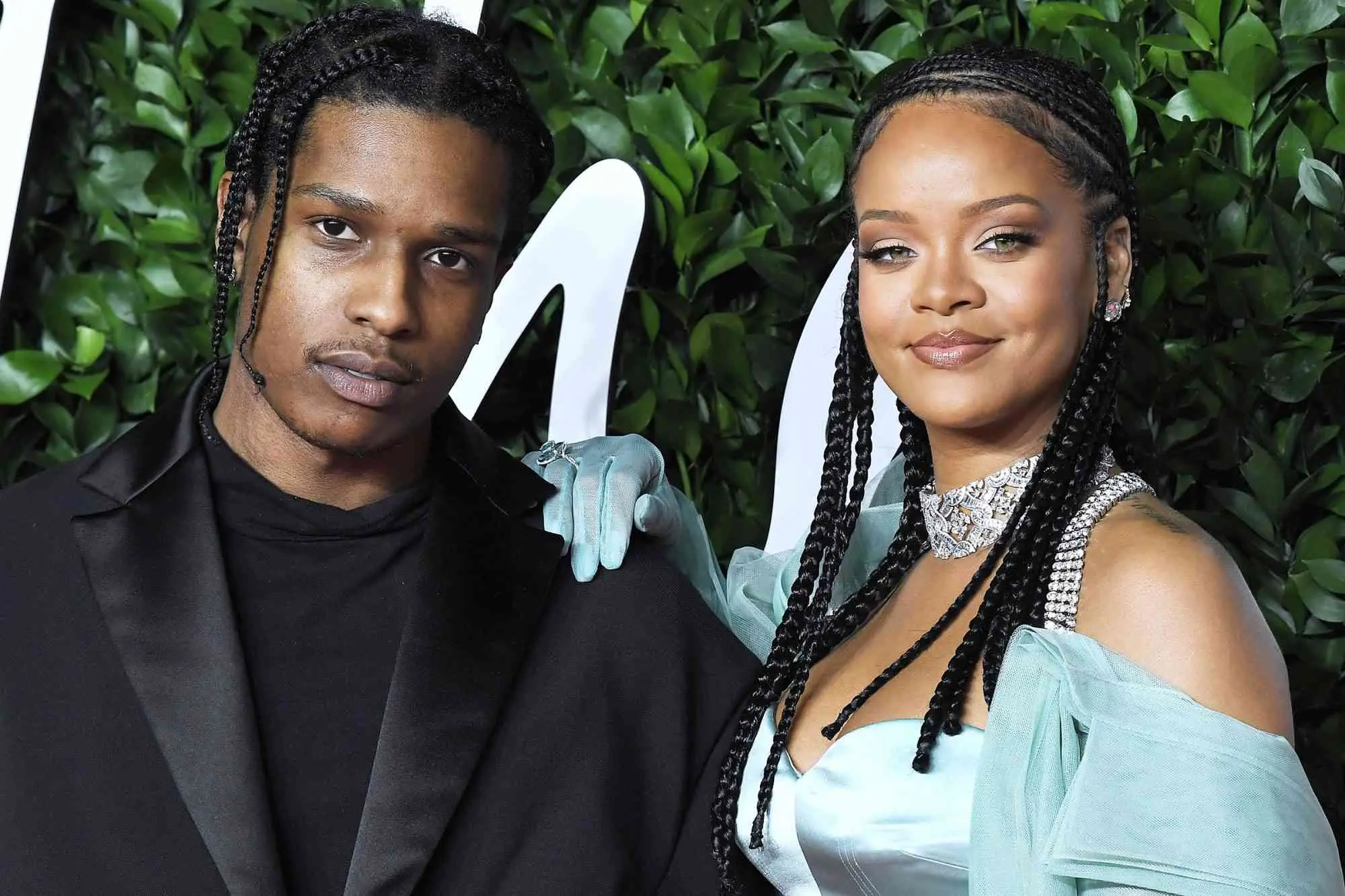 Rihanna and A$AP Rocky posing together at a formal event, with Rihanna wearing a light blue dress and jewelry.